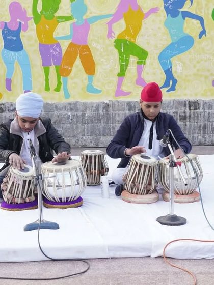 Two students performing a tabla piece with microphones, ready for an audience. This prepares them for professional sound setups.