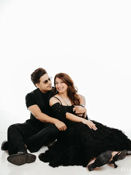 A relaxed and intimate portrait of a couple sitting on the floor against a clean white backdrop. This minimalist studio setup allows their connection and stylish black attire to be the main focus, creating a timeless and elegant pre-wedding photograph.