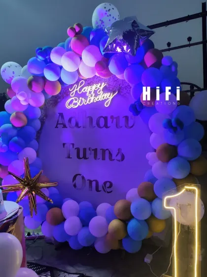A stylish outdoor birthday setup for a first birthday, featuring a multi-colored balloon circle and neon signs.