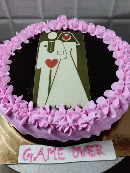 A playful "Game Over" cake for a wedding celebration. This chocolate cake is decorated with pink buttercream and a fun bride and groom graphic.
