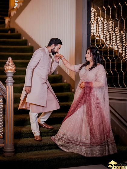 Capturing a moment from a Roka ceremony on a grand staircase. The groom's chivalrous gesture of kissing her hand adds a touch of classic romance to their celebration.