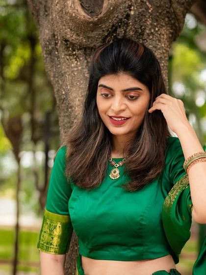 A graceful outdoor portrait of a woman in a green saree. The natural setting complements the traditional attire perfectly.