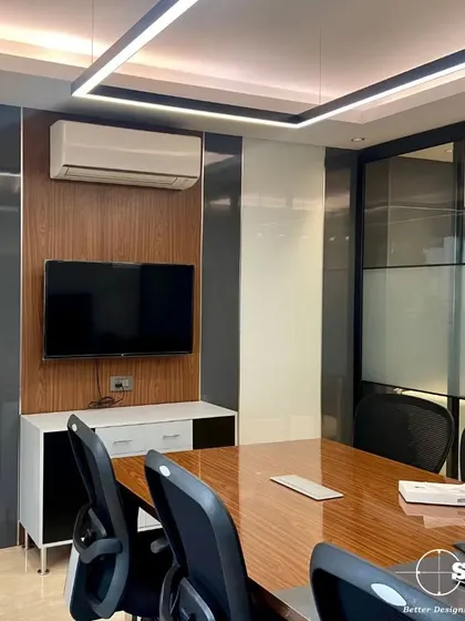 A sleek and modern conference room. The design features a large wooden table, comfortable office chairs, and a wall-mounted TV, with linear overhead lighting and high-gloss wall panels.
