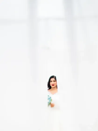 A minimalist bridal portrait, with the bride peeking through a gap in white curtains. This creates a sense of mystery and elegance.