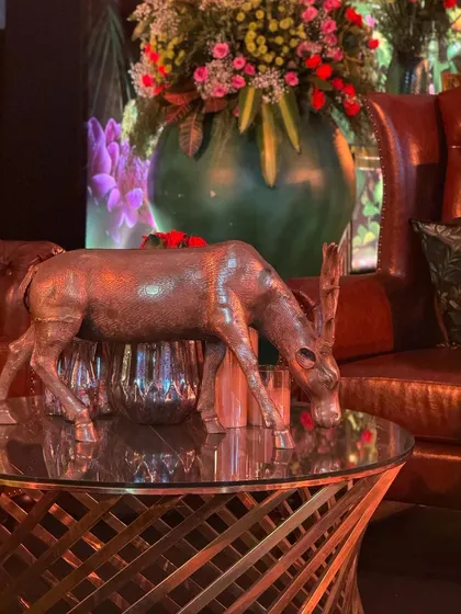 The allure of a mood-lit night. A close-up of a decor detail from our "Jungle" themed party, featuring a brass deer sculpture on a modern glass table.