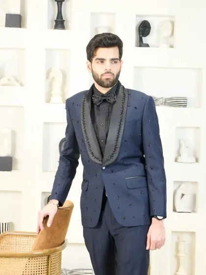 A commanding presence is guaranteed in this navy blue tuxedo. The jacket features exquisite black beading along the shawl collar and is scattered across the body, offering a sophisticated and textured look for any black-tie affair.