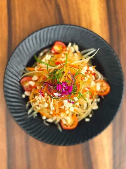 The vibrant and refreshing Thai Papaya Salad, beautifully garnished with an edible flower, is a cornerstone of our authentic Thai menu.