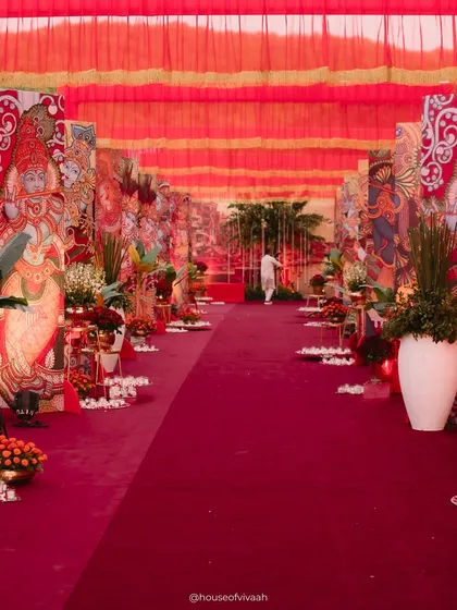 The long, dramatic aisle leading to the wedding area, flanked by large, hand-painted panels depicting traditional Indian art, creating an immersive cultural experience for guests.