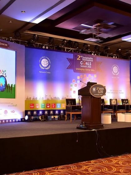 The stage for a corporate goals summit, featuring multiple screens for branding and presentations. The setup is professional and designed to facilitate a large-scale conference with multiple speakers.
