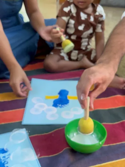 The simple act of dabbing paint with a sponge becomes a moment of connection. The parent's hand guiding the child's shows them new skills in a supportive and loving way.