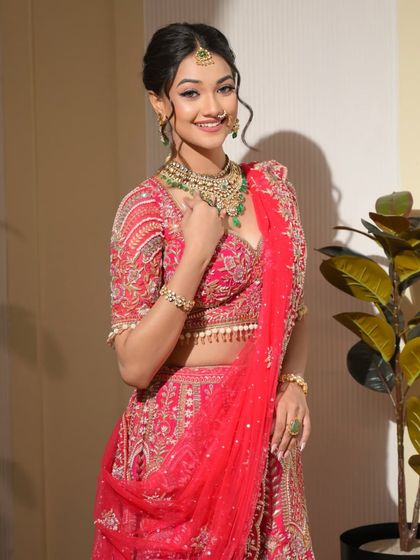 A full-length shot showcasing the stunning red lehenga and the bride's confident and graceful posture. The makeup ties the entire look together.