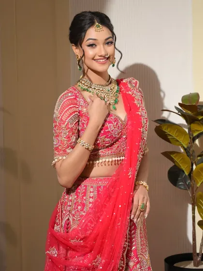 A full-length view of this stunning red lehenga look. It’s a perfect example of a classic bridal style with a contemporary, fresh-faced makeup application.