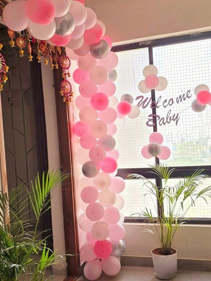 A simple and elegant balloon garland in pink, white, and silver for a 'Welcome Baby' home decoration.