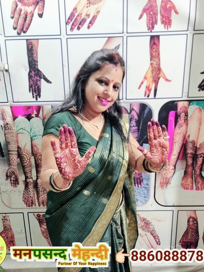 A happy client showing her beautiful Karwa Chauth mehndi in front of our design wall.