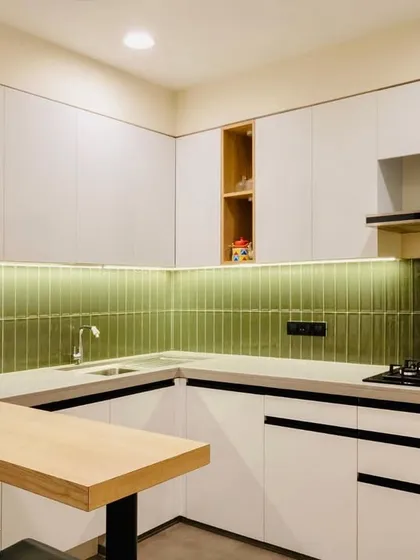 A fresh and modern kitchen with white cabinets, a light wood breakfast bar, and a vibrant green tiled backsplash that adds a pop of color.