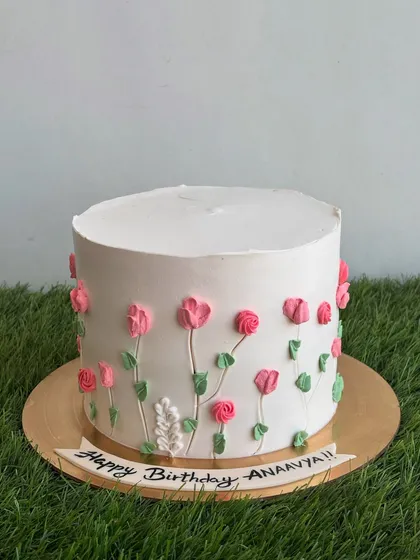 Our spring-themed cake with piped pink flowers on a clean white whipped cream base. This design is made with an eggless whole wheat jaggery cake inside.