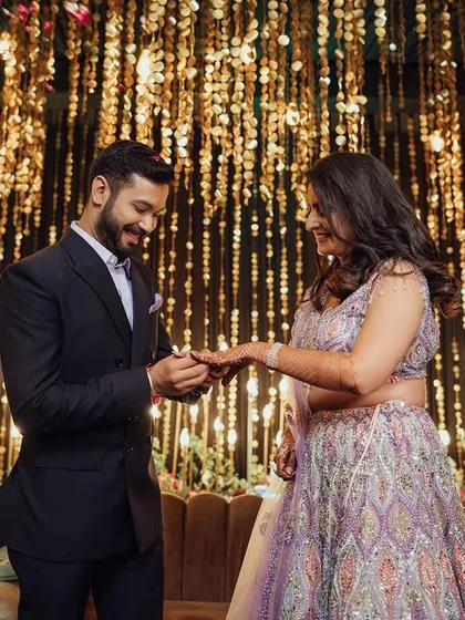 The ring exchange. A classic, happy moment from an engagement ceremony, captured against a glittering backdrop of fairy lights.
