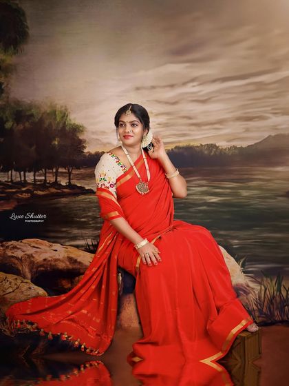 A lovely portrait capturing the elegance of a traditional red saree and floral hair adornment. The soft, painted background creates a dreamy, romantic atmosphere.