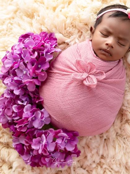 A lovely portrait with a baby in a pink wrap, with a trail of purple flowers adding a pop of color and visual flow.