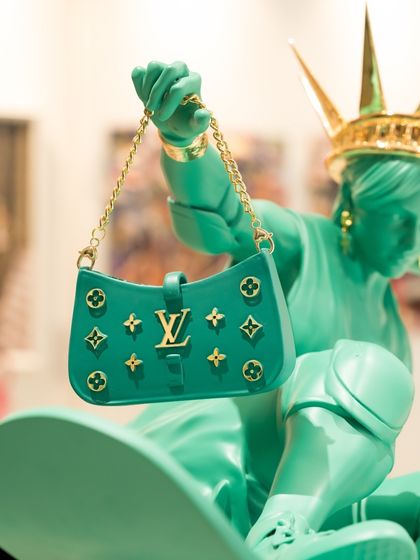 A close-up of the monogrammed luxury bag held by the modern-day Lady Liberty, a key element of her reimagined identity.