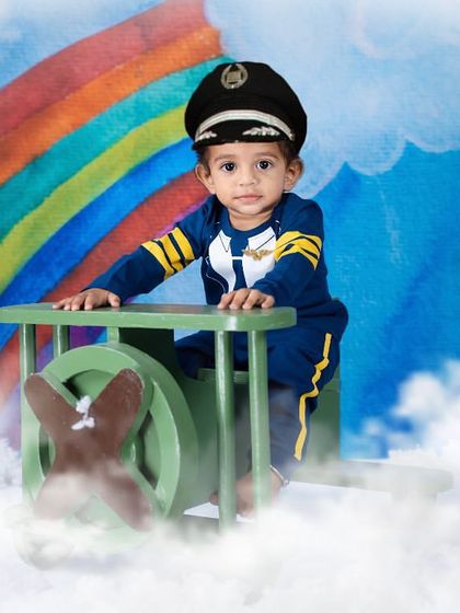 Ready for takeoff! This little pilot is flying high above the clouds in his own airplane, with a rainbow in the background for a touch of magic.