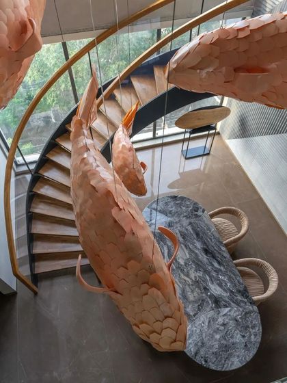 An overhead view reveals the scale of the fish light installation as it hangs above the marble dining table, spiraling down from the ceiling.