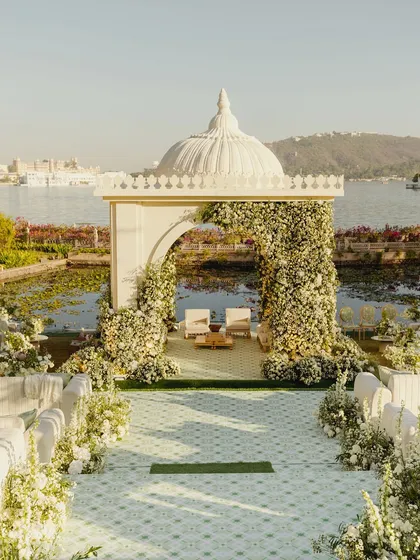 A serene mandap that appears to float on the waters of Udaipur. Framed by an arch of white florals, this design blends timeless tradition with the natural beauty of the location, creating a tranquil and elegant space for vows.