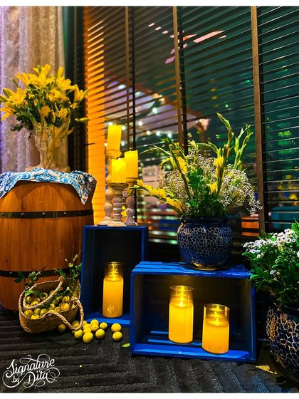 I often use rustic elements like wooden barrels and crates to add texture and height to my decor. Here they are used to display floral arrangements and candles, enhancing the Sicilian theme.