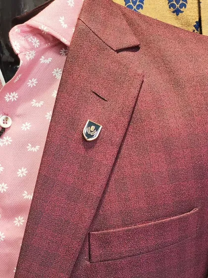 The difference is in the details. A close up of a wine colored, self textured suit fabric paired with a delicate lapel pin. It's these small, personalized touches that elevate an outfit from good to great.
