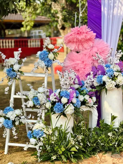A detailed look at the floral decor for a colorful Haldi entrance, featuring blue hydrangeas, white flowers, and large pink paper pom-poms.