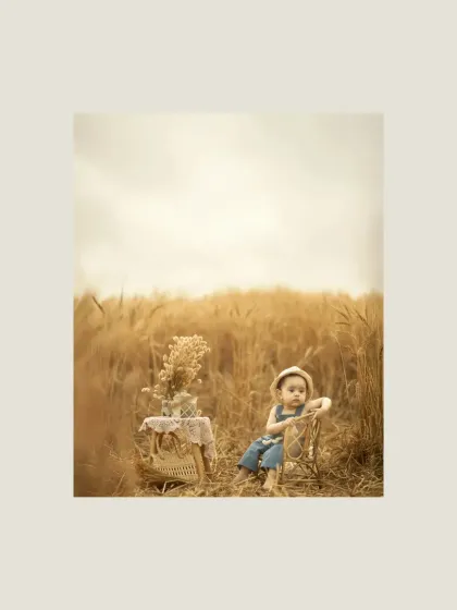 A wide shot showing the child and the picnic setup in the middle of the golden field. This image captures the scale and beauty of the natural surroundings, creating a dreamy and picturesque scene.
