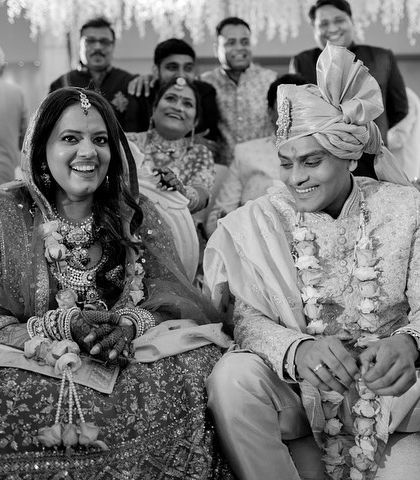 A candid black and white shot of the couple sharing a laugh with their family during the ceremony. It captures the relaxed and happy atmosphere of their special day.