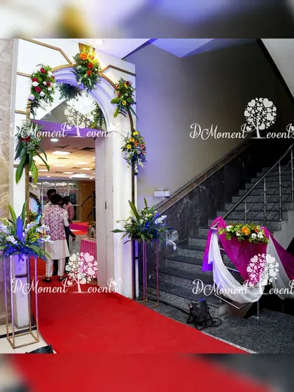 The red carpet entrance for the 50th anniversary celebration. The entryway is adorned with elegant floral arrangements on pedestals, setting a sophisticated tone for the event.