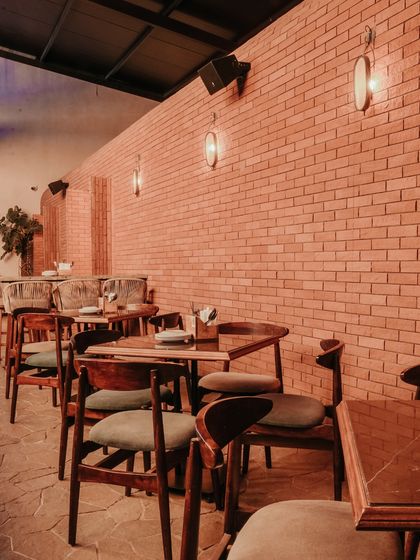 This section of the restaurant features a long, exposed brick wall with minimalist wall sconces. The simple wooden tables and chairs create a rustic and intimate dining atmosphere.