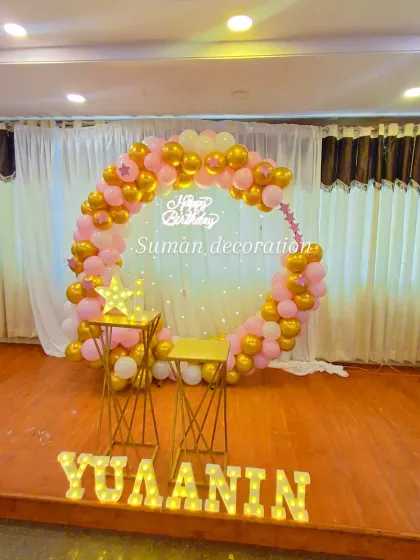 A simple yet elegant stage setup for a birthday. It features a circular balloon arch in pink and gold, a neon sign, and personalized marquee letters.