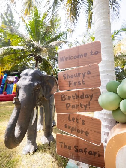 A rustic wooden signpost directing guests to "explore the safari" at Shourya's first birthday party, complete with an elephant prop.