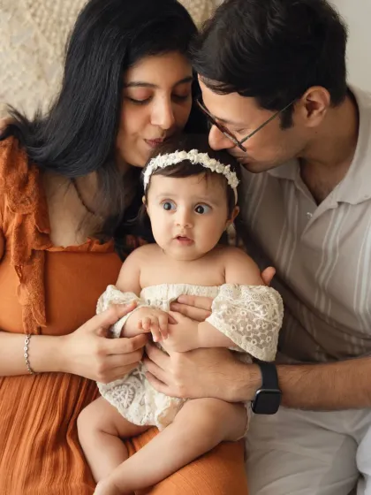 A sweet family portrait with a curious baby girl held by her parents. The parents' loving kisses frame their daughter beautifully.