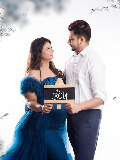 A proud gender reveal moment for the couple. They stand together in a dreamy, light-filled setting, holding a sign that says 'It's a Boy'.