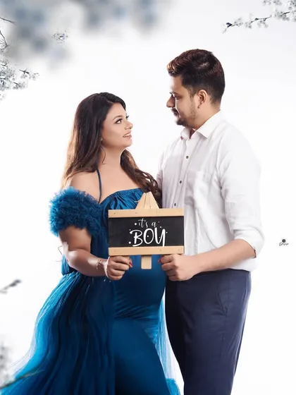 A proud gender reveal moment for the couple. They stand together in a dreamy, light-filled setting, holding a sign that says 'It's a Boy'.