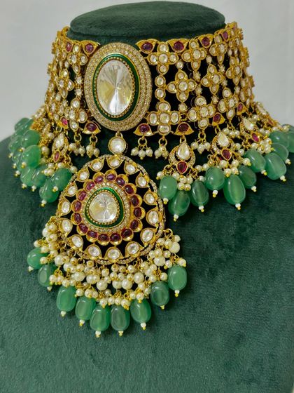 A heavy bridal choker with a large pendant, featuring intricate Kundan work and green bead drops. This rental piece is designed to be the centerpiece of your bridal attire.