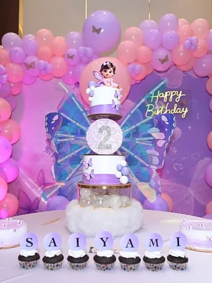 The full dessert table setup for Saiyami's butterfly-themed second birthday. It includes the main tiered cake, smaller cakes, and personalized cupcakes.