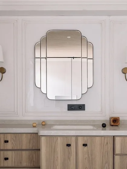 The vanity area in the den's bathroom features a beautiful art-deco inspired mirror and custom wooden cabinetry. The design is clean, elegant, and timeless.