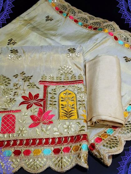 A festive unstitched dress material in a cream color. The top fabric features colorful embroidery depicting a traditional design, paired with a multi-colored gota patti border dupatta.