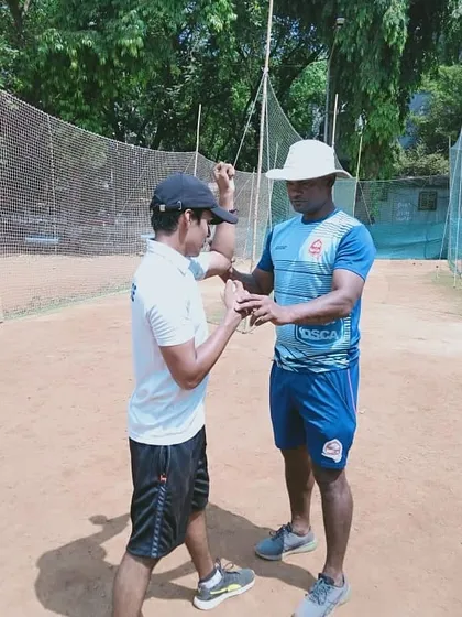 Correcting the elbow position of a young bowler. A straight arm at the point of delivery is vital for legal and effective bowling.