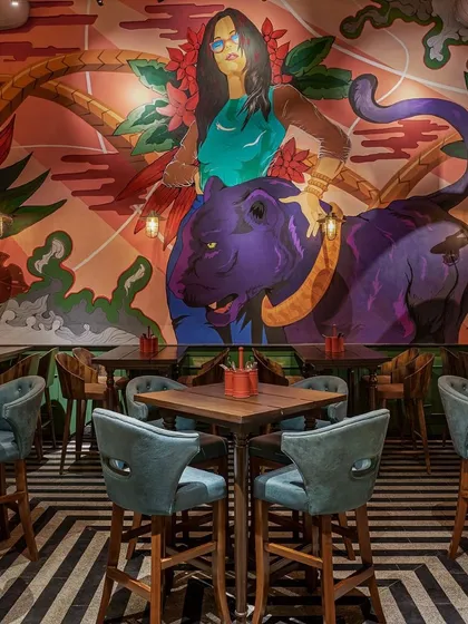 This powerful mural features a woman with a purple panther, set against a tropical-themed background. The bold colors and dynamic composition make it a commanding feature wall in this trendy restaurant.