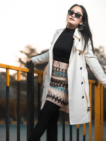 A classic winter fashion look. The makeup is polished and understated, allowing the stylish white trench coat, sunglasses, and patterned skirt to take center stage.