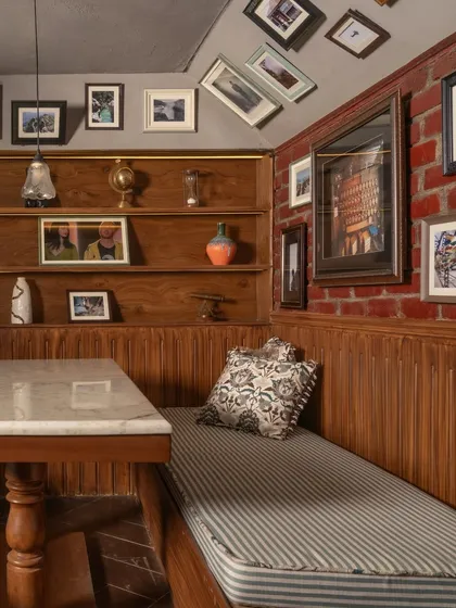 A detail of the booth seating, showing the texture of the brick wall, the warmth of the wood paneling, and the eclectic collection of framed art. Every element is chosen to make the space feel lived-in and unique.