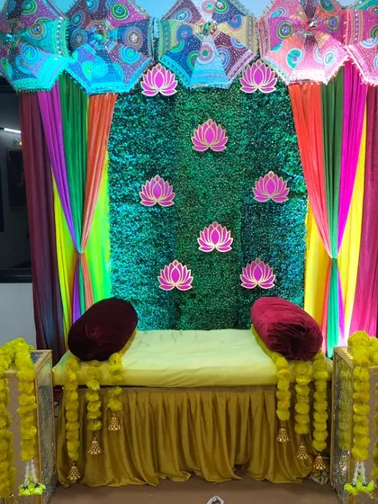 We create authentic and vibrant Haldi ceremony decorations. This setup features a lush green grass wall backdrop, decorated with lotus cutouts and colorful drapes, traditional umbrellas (chhatris), and marigold garlands (genda phool) for the seating area.