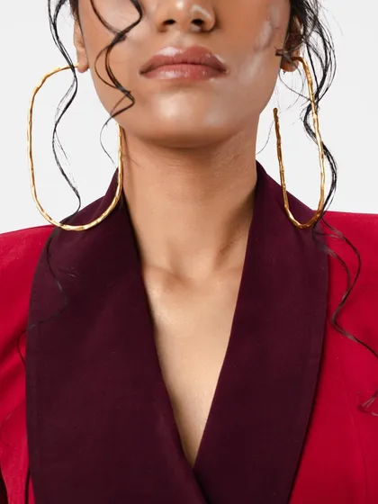 A close-up on the makeup and hair for a high-fashion shoot. The look features dewy skin, a nude lip, and wet-look hair tendrils framing the face, paired with oversized statement earrings.