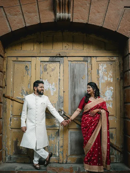 A classic portrait of the couple in front of a vintage yellow door. Their contrasting red and white outfits pop against the rustic background, creating a visually stunning image.